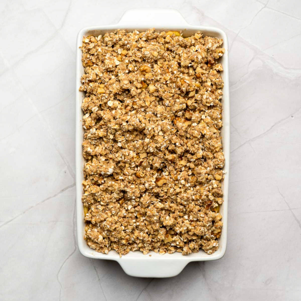 Baking dish with apple crisp before baking, topped with oat and nut crumble.
