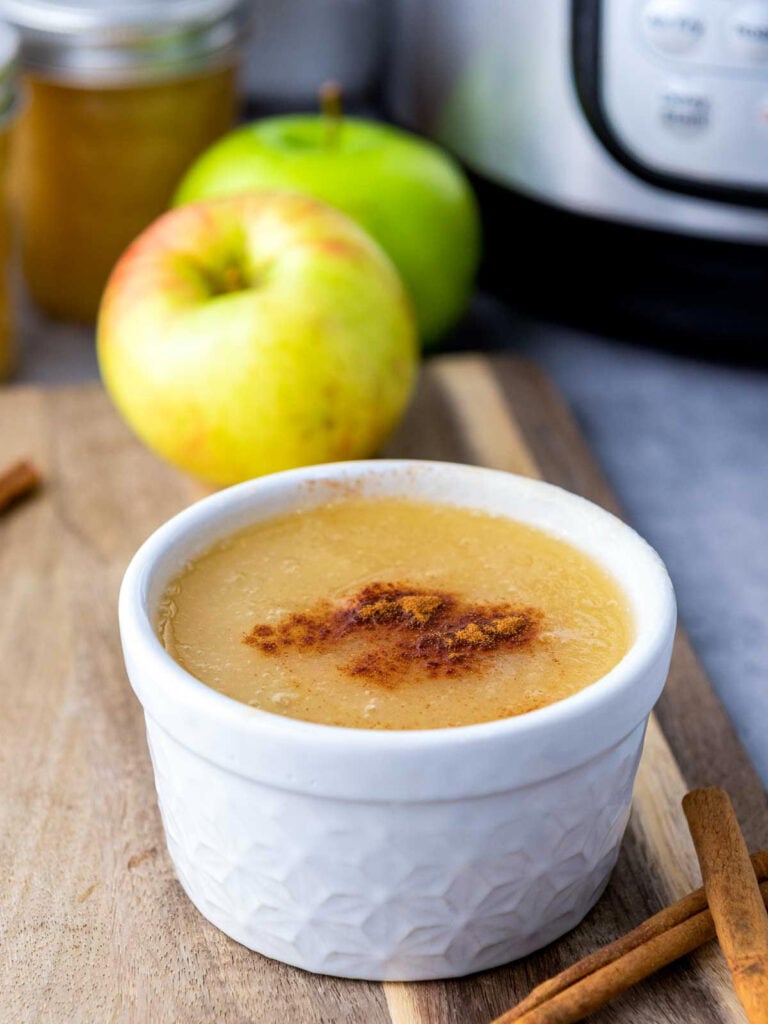 Bowl of homemade Instant Pot applesauce topped with cinnamon, surrounded by apples and jars.