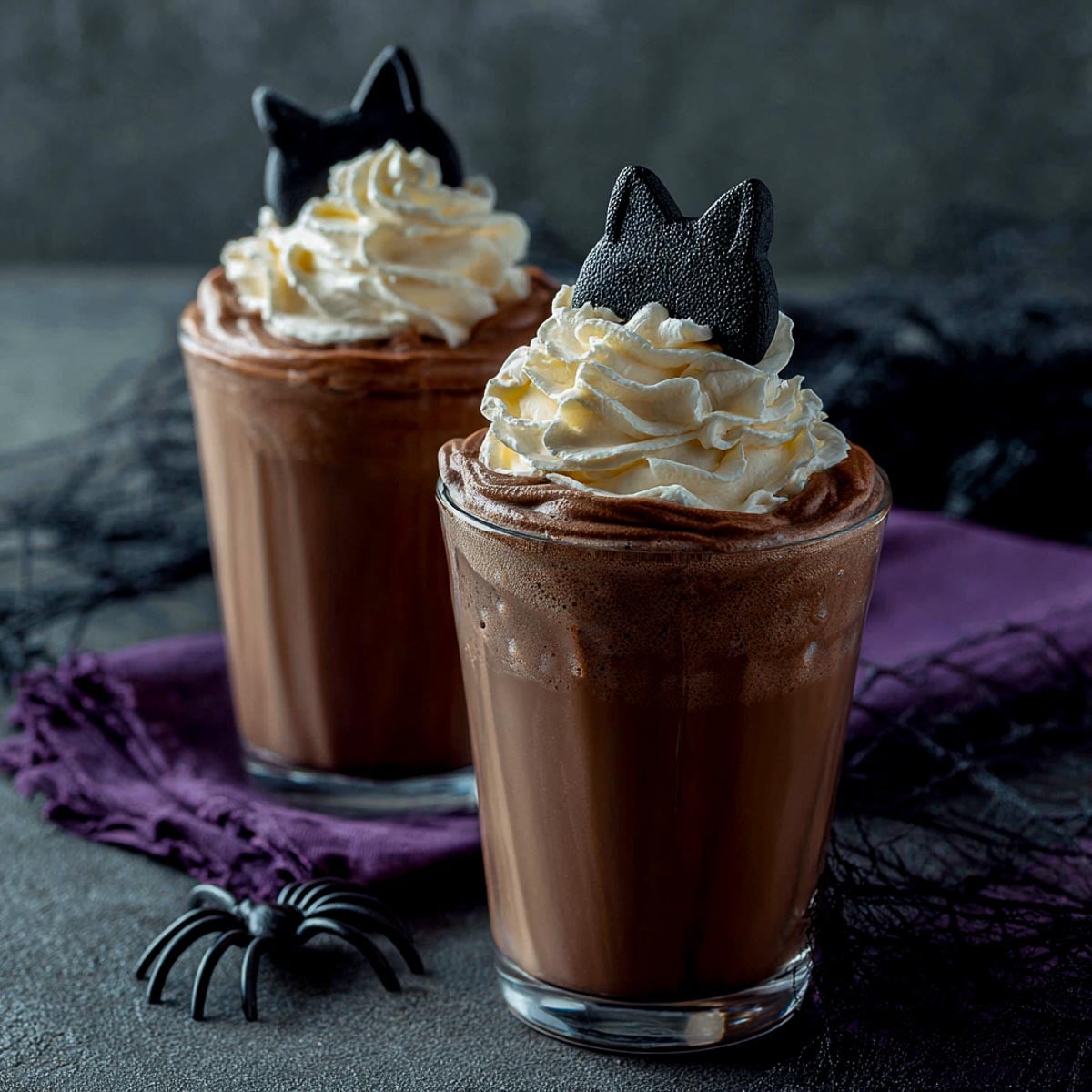 Two chocolate milk drinks topped with whipped cream and black cat fondant toppers