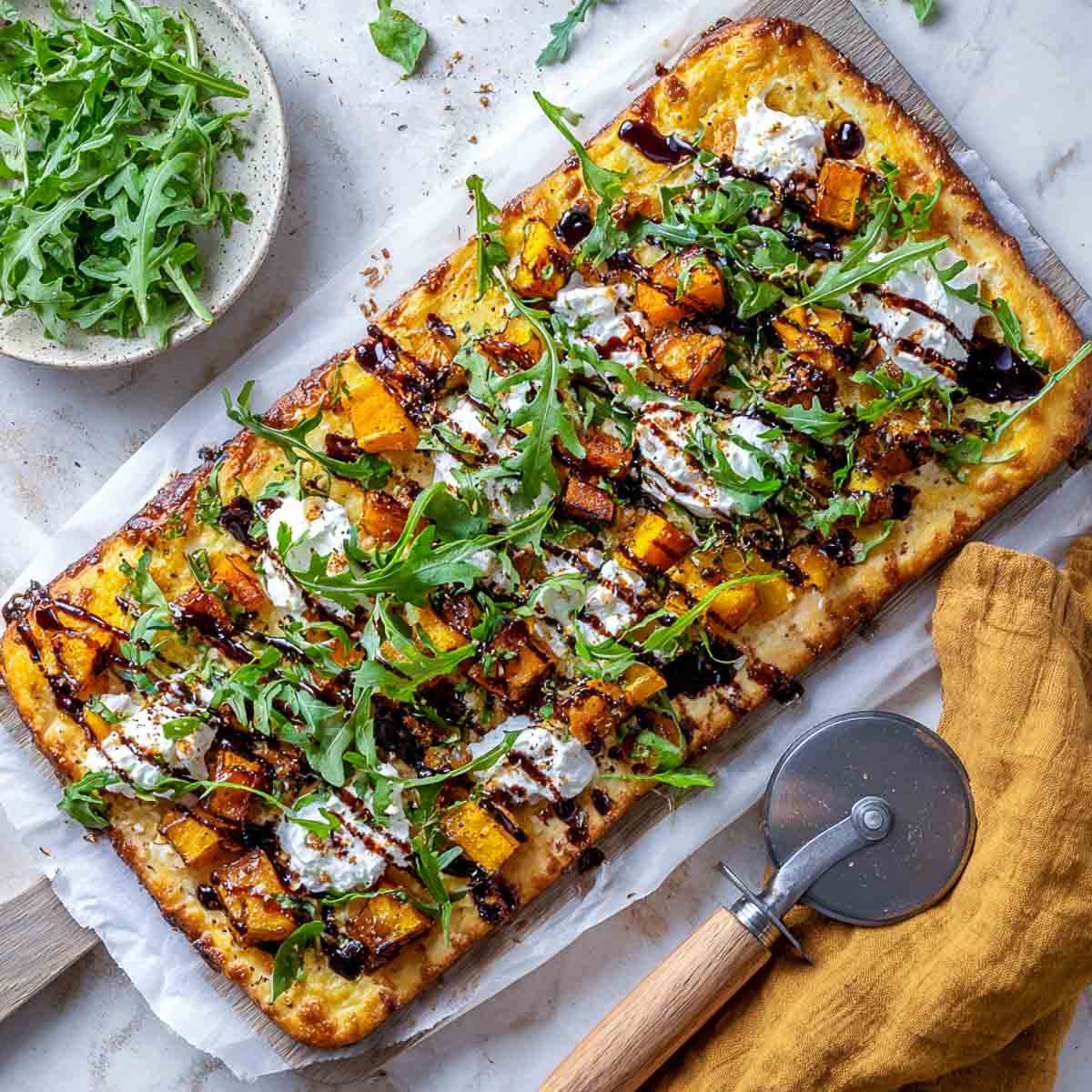 Flatbread topped with roasted squash, dairy-free cottage cheese, arugula, and balsamic glaze.