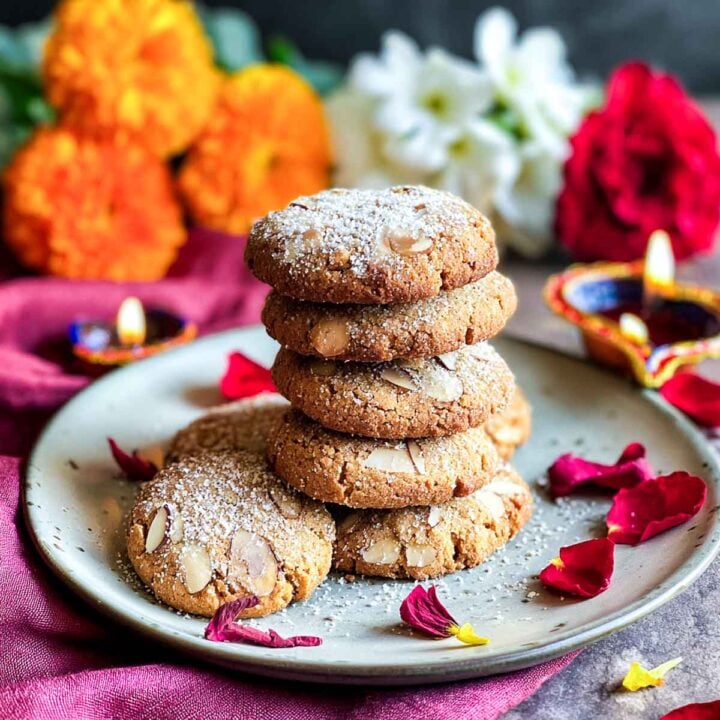 Stack of chai-spiced almond cookies dusted with sugar on festive plate.