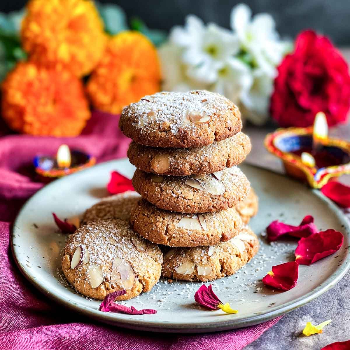 Stack of chai-spiced almond cookies dusted with sugar on festive plate.