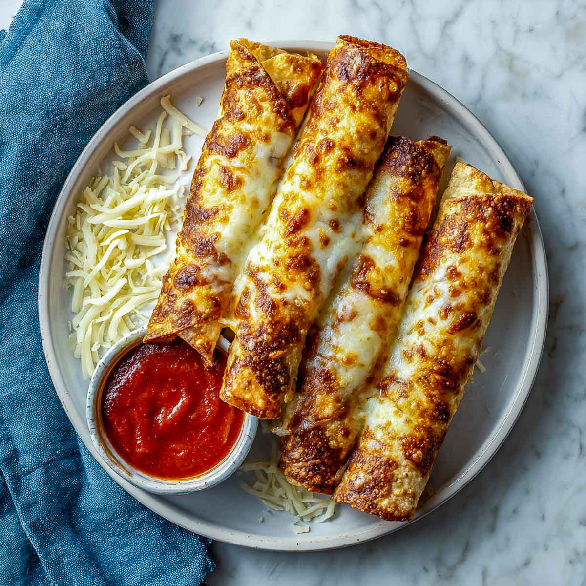 Crispy cheese crispitos on a plate with marinara and shredded cheese.