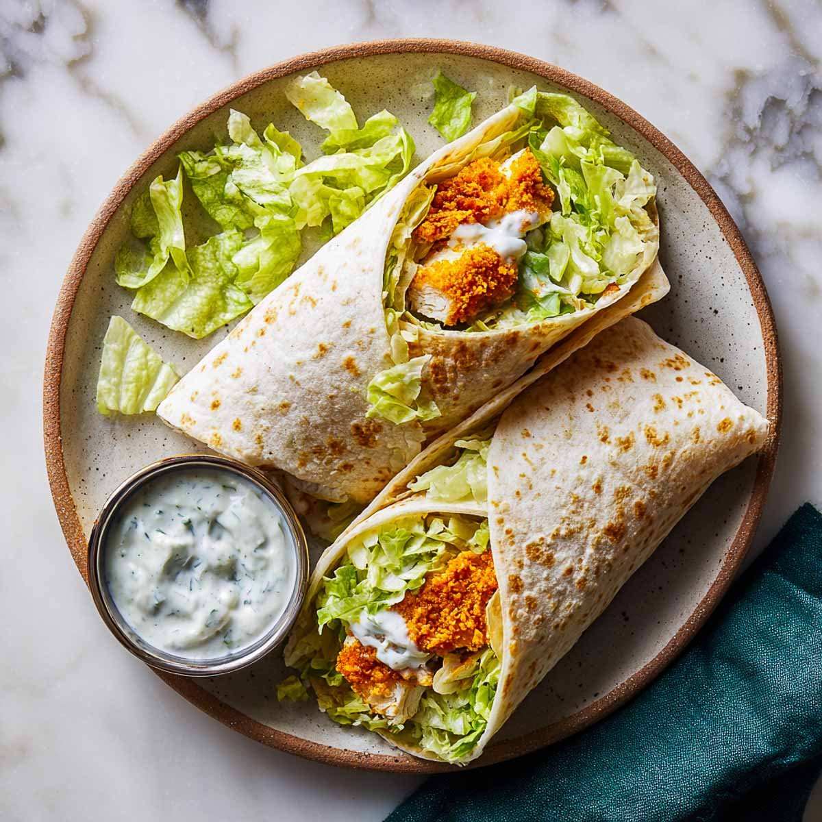 Top-down view of two crispy chicken ranch wraps on a ceramic plate with lettuce and ranch dip.