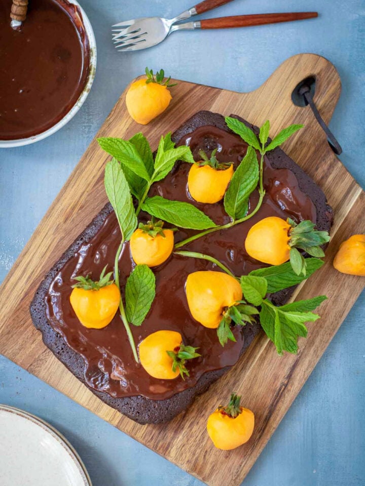Overhead view of whole chocolate brownie cake decorated with orange-dipped strawberries and mint leaves to resemble a pumpkin patch.