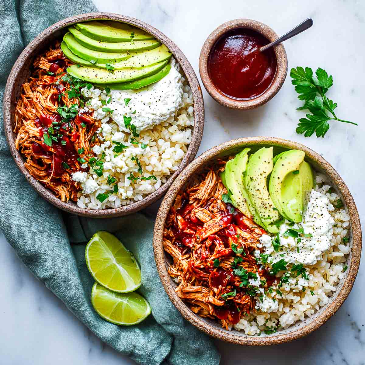 Two BBQ chicken and cottage cheese bowls with avocado, rice, and parsley.