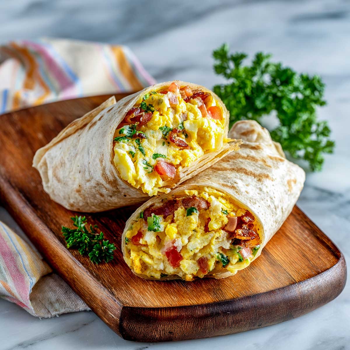Two breakfast burritos filled with eggs, bacon, and parsley, sliced on a wooden board.