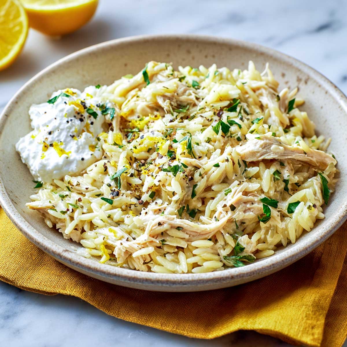 A bowl of creamy lemon herb orzo with shredded chicken and herbs.