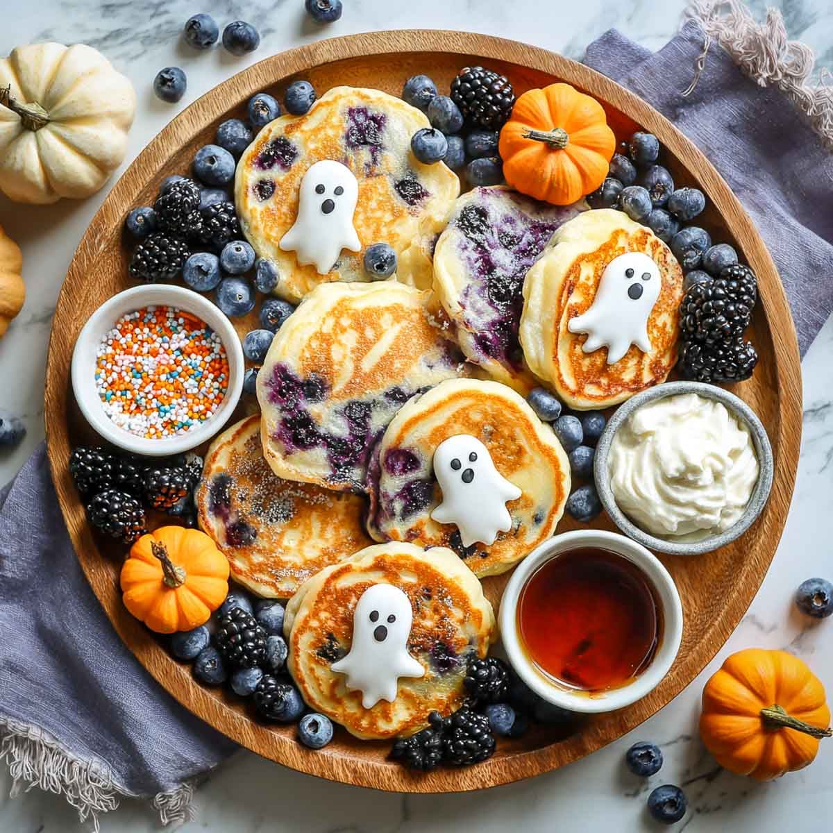 Whimsical Halloween breakfast board with fluffy blueberry pancakes topped with small white ghost decorations.