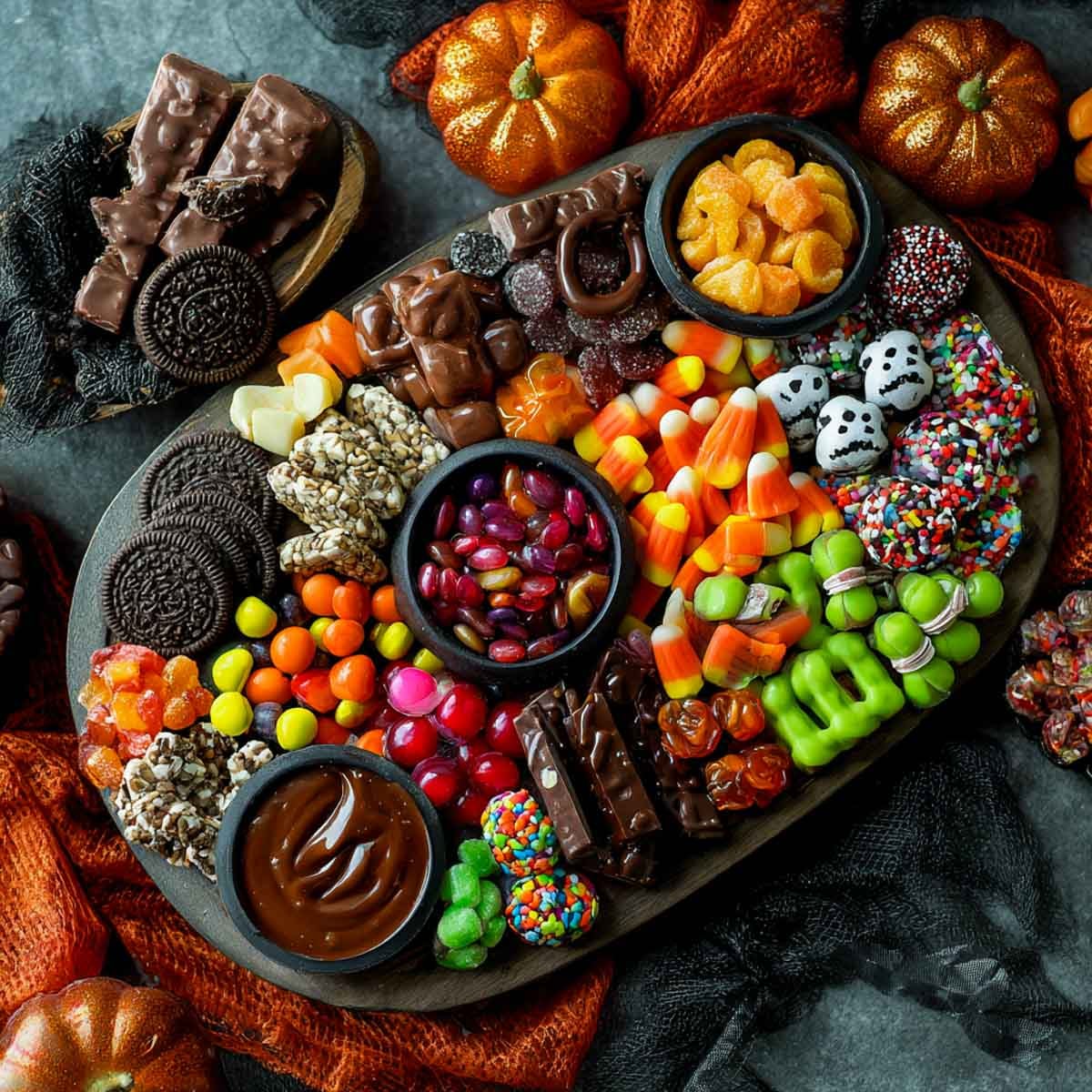 Halloween candy charcuterie board with candy corn, chocolate bars, jelly beans, ghost-shaped marshmallows, caramel dip, assorted gummies, green Halloween candies.