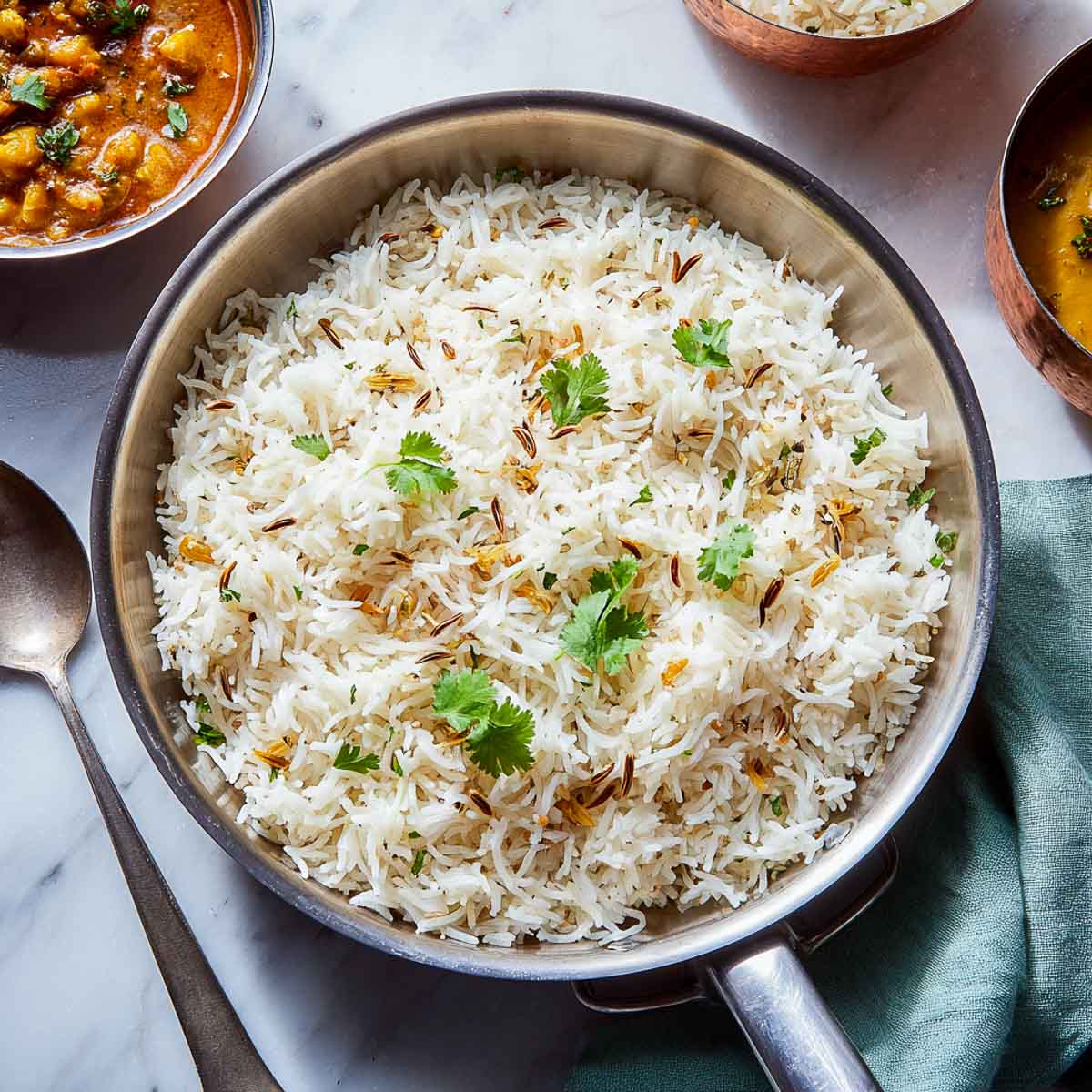 Pan of jeera rice with golden cumin seeds and cilantro leaves.
