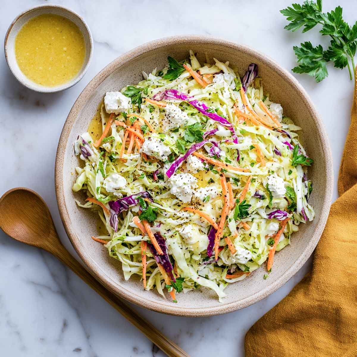 Shredded cabbage slaw with carrots, herbs, and cottage cheese on marble surface.