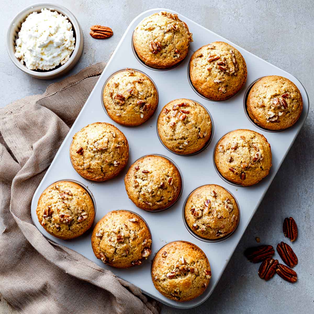 Golden maple pecan cottage cheese muffins in a muffin tin, with pecans and a bowl of cottage cheese on the side.