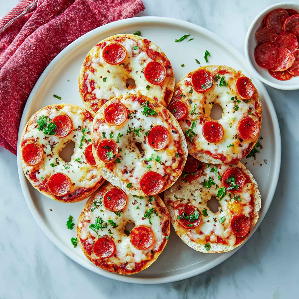 Top-down shot of six mini bagel pizzas topped with melted mozzarella, pepperoni, and parsley.
