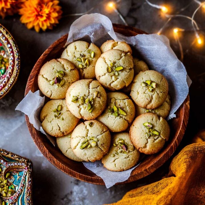 Wooden bowl filled with golden nankhatai cookies sprinkled with pistachios.