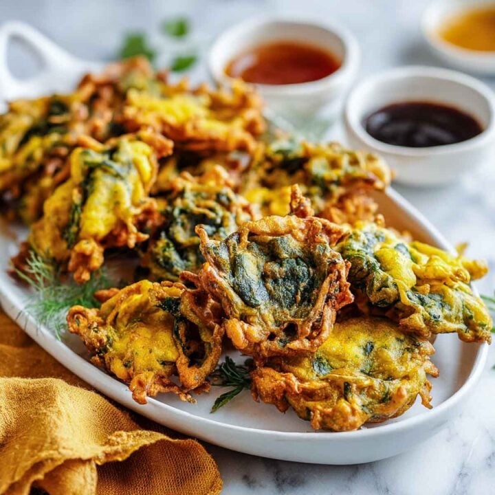 Crispy palak pakoras served on a platter with chutney dips.
