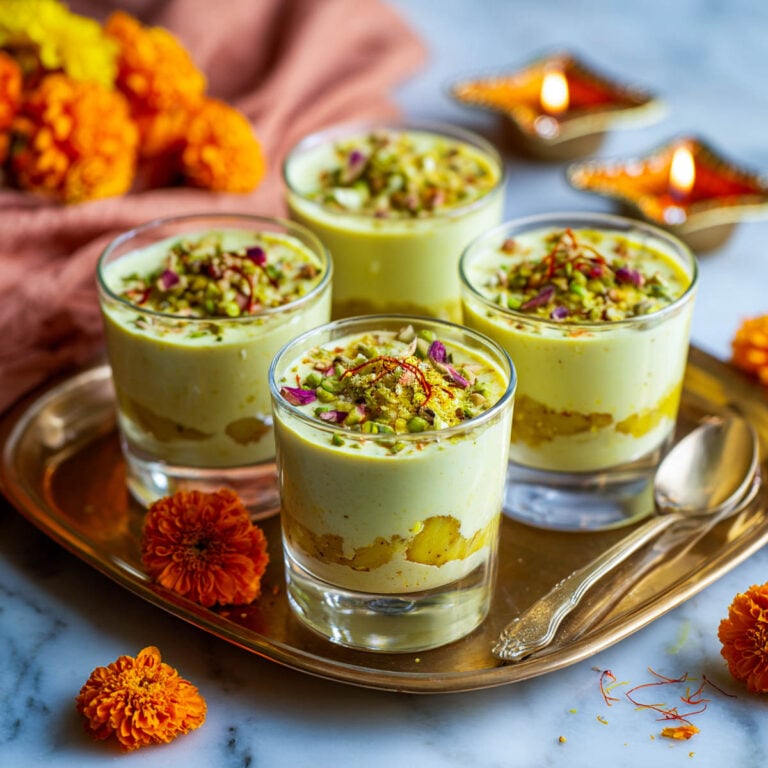 Four glass cups of Ras Malai mousse with pistachios, saffron, and rose petals on a brass tray.
