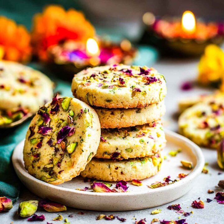 Stack of rose pistachio shortbread cookies topped with petals and nuts.