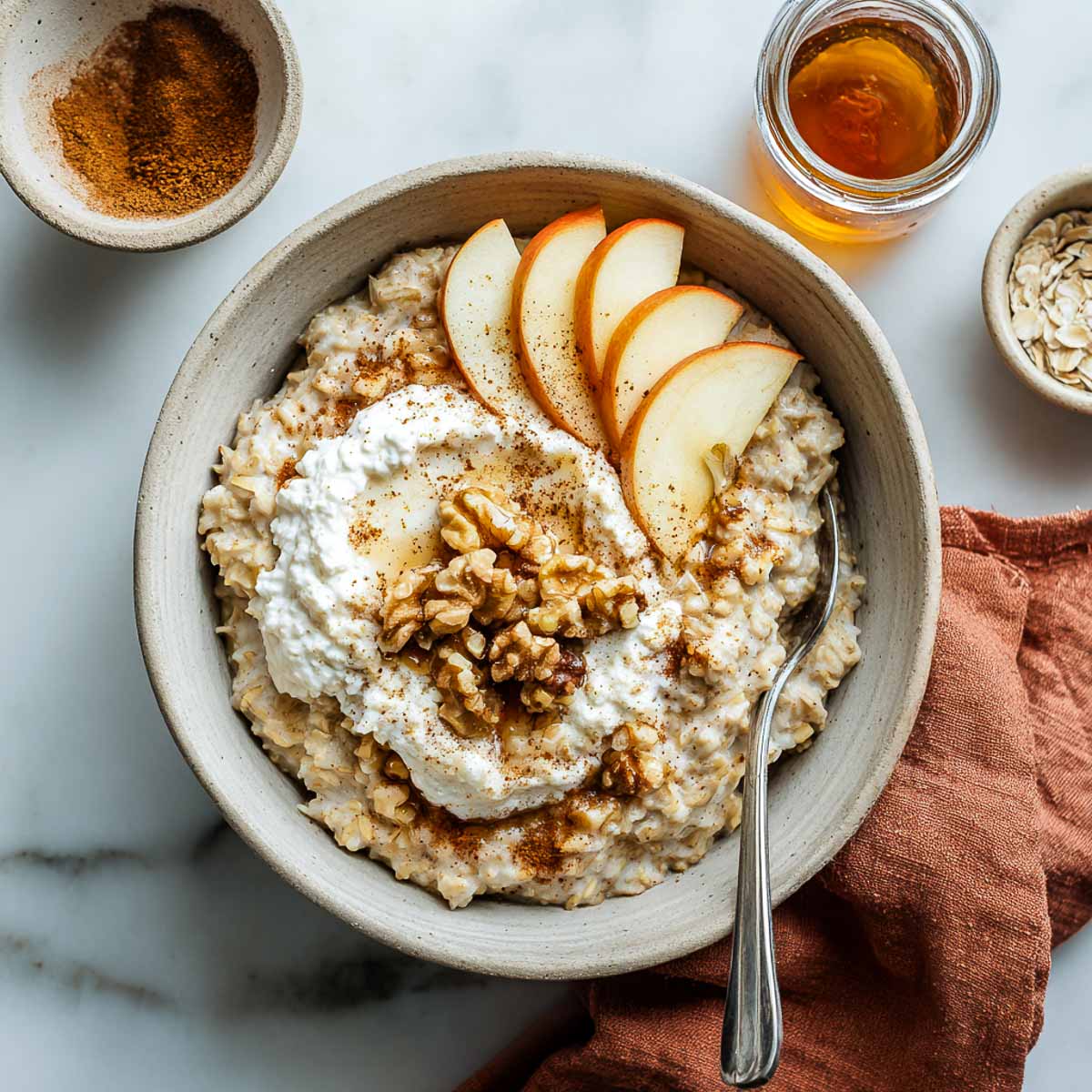 Bowl of apple cinnamon oats topped with vegan cottage cheese, apples, walnuts.