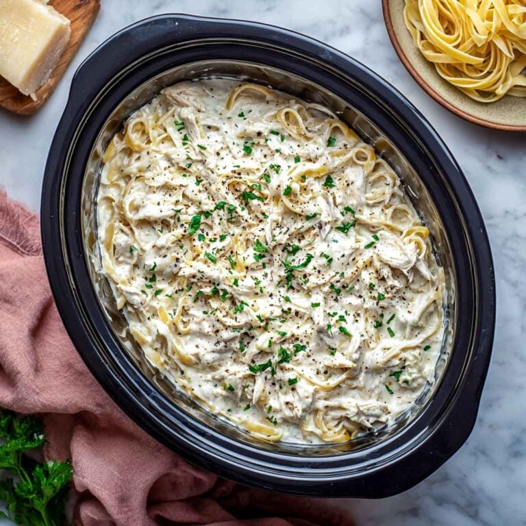 Creamy chicken alfredo with cottage cheese and fettuccine in a black crockpot.