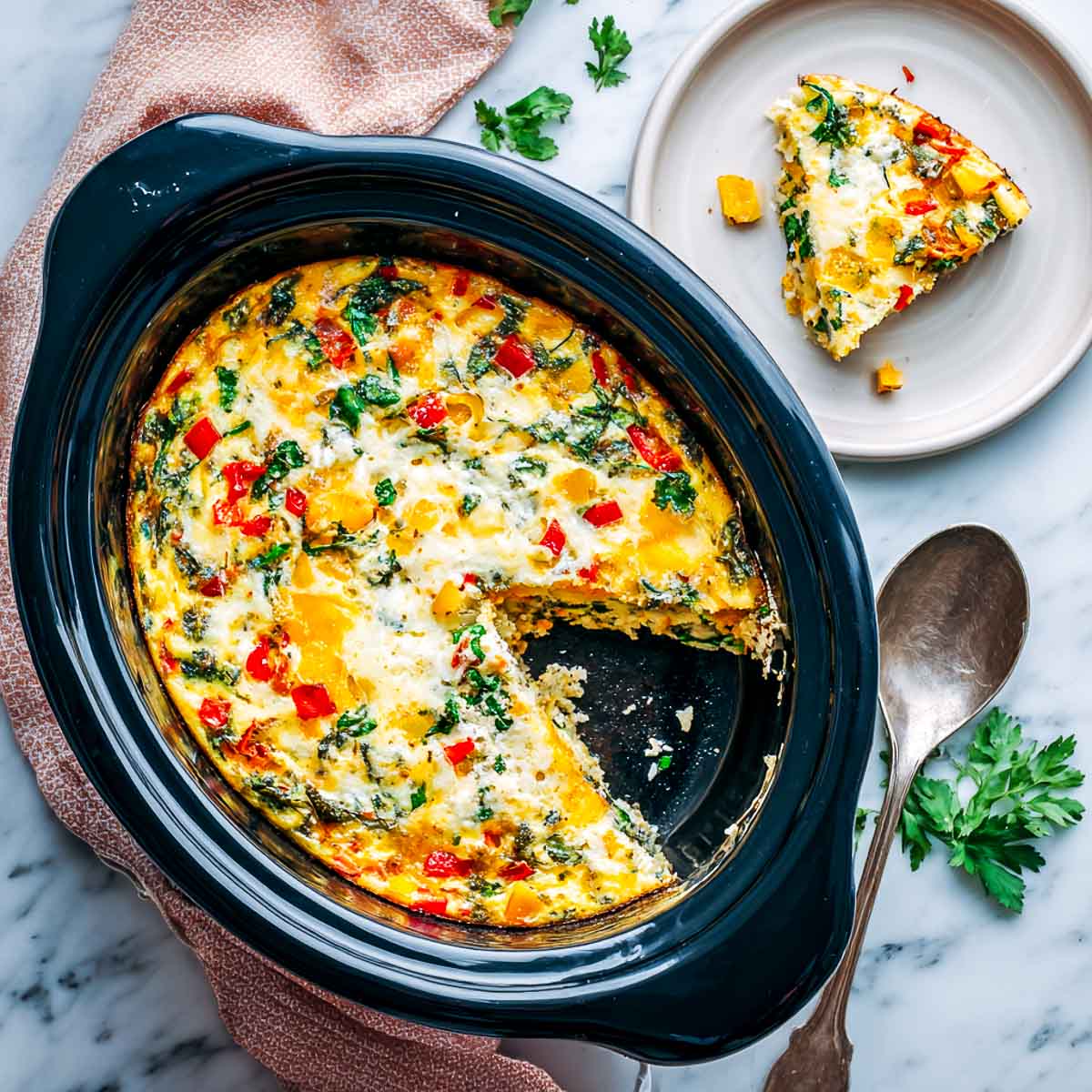 Top-down view of a slow cooker egg casserole with cheese and colorful vegetables, one slice served on a white plate.