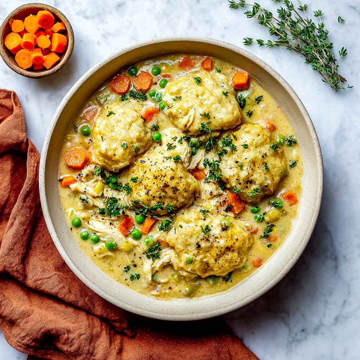 Bowl of vegan chicken and dumplings with golden dumplings, vegetables, and creamy broth.