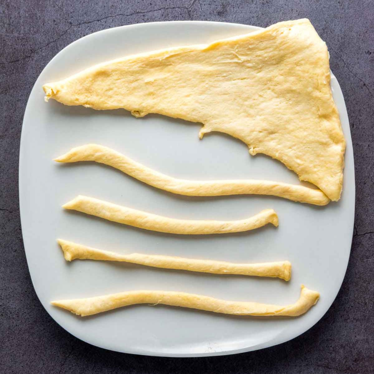 Crescent roll dough triangle sliced into thin strips on white plate.