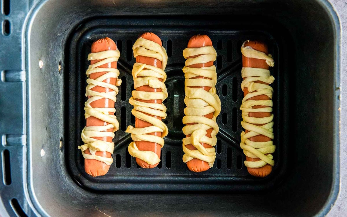 Wrapped hot dogs placed in air fryer basket before cooking.