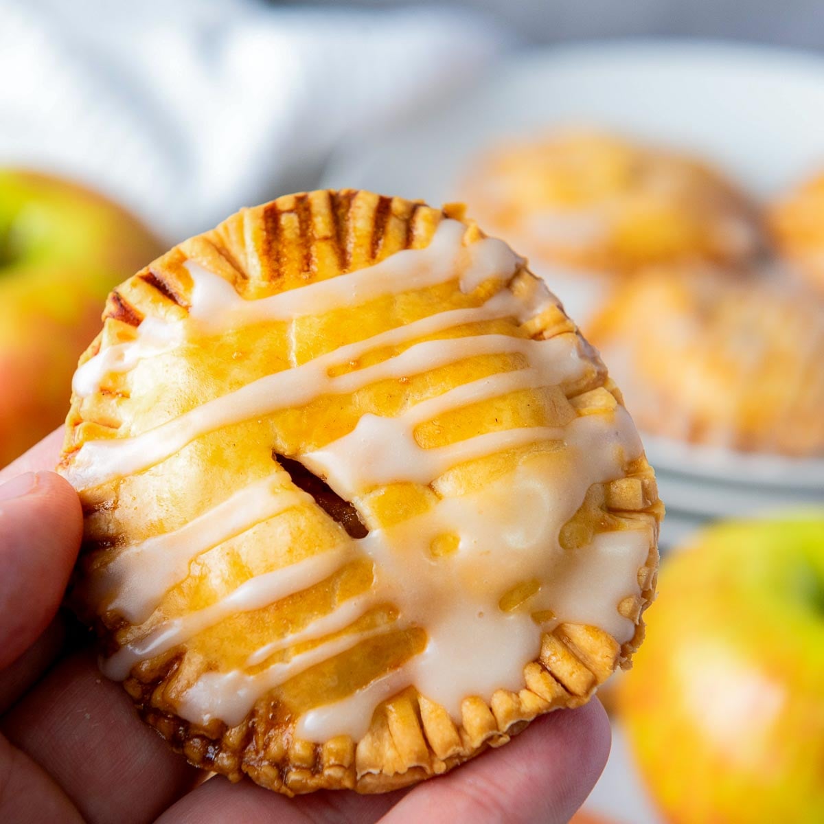 Hand holding a glazed apple hand pie with flaky crust and sweet icing drizzle.