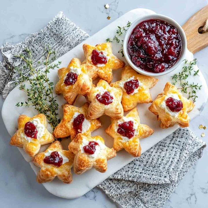 Golden puff pastry stars filled with goat cheese and topped with cranberry sauce on a marble platter.