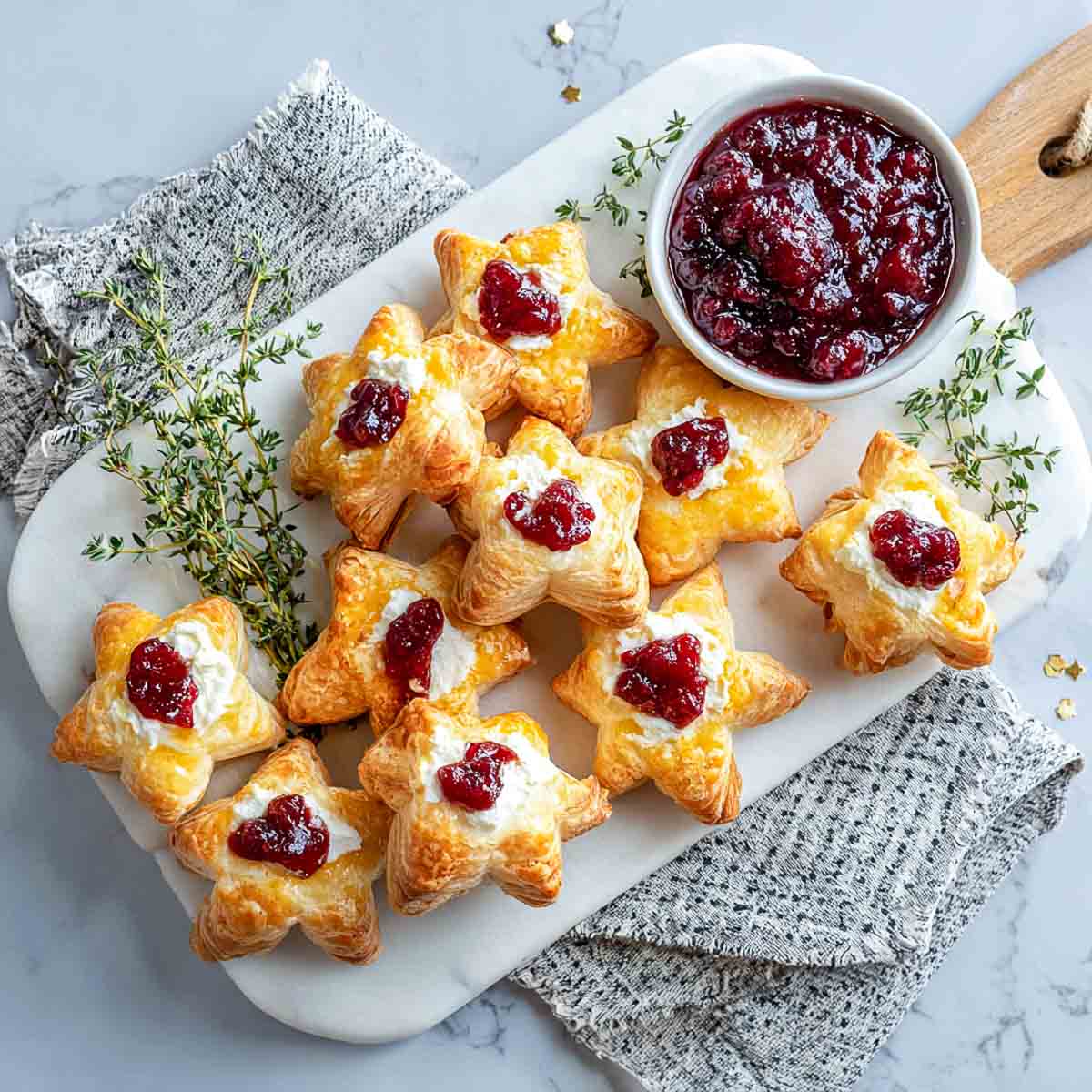 Golden puff pastry stars filled with goat cheese and topped with cranberry sauce on a marble platter.