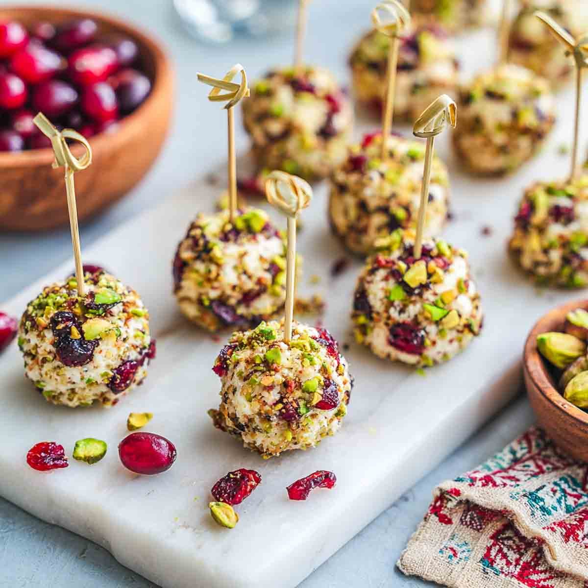 Mini vegan cheese ball bites rolled in cranberries and pistachios with cocktail picks.