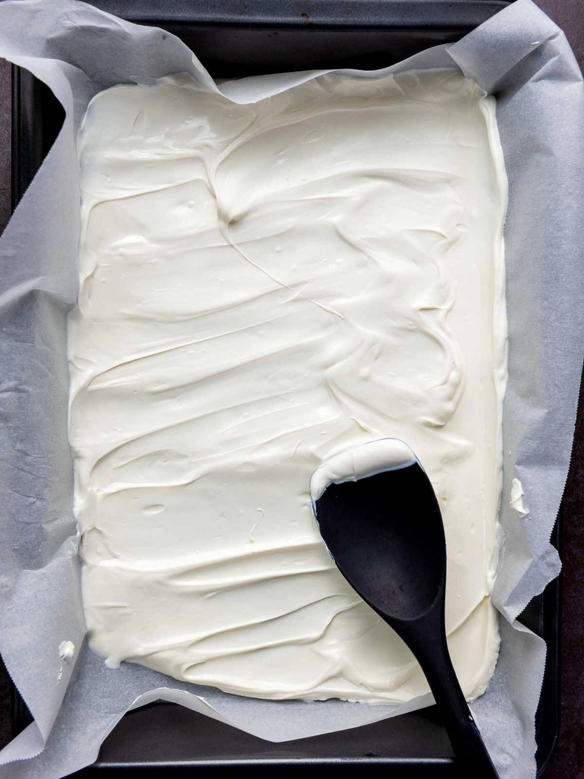 White melted chocolate spread evenly in parchment-lined baking pan.