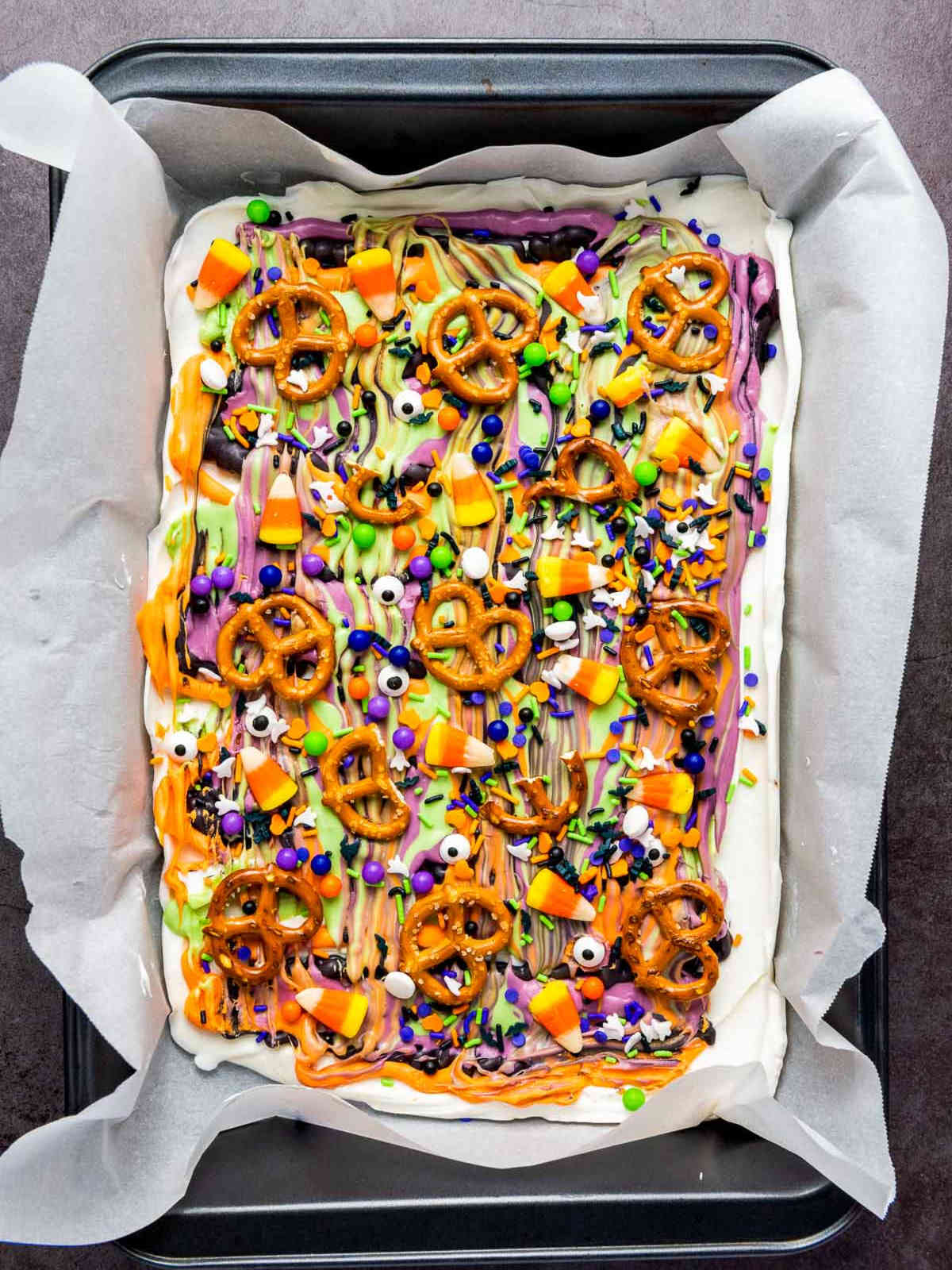 Finished Halloween candy bark topped with pretzels, sprinkles, and candy corn.