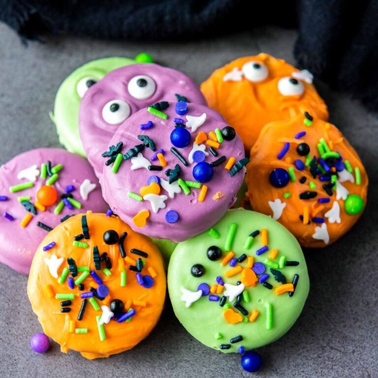 Colorful Halloween Oreo treats decorated with sprinkles and candy eyes on table.