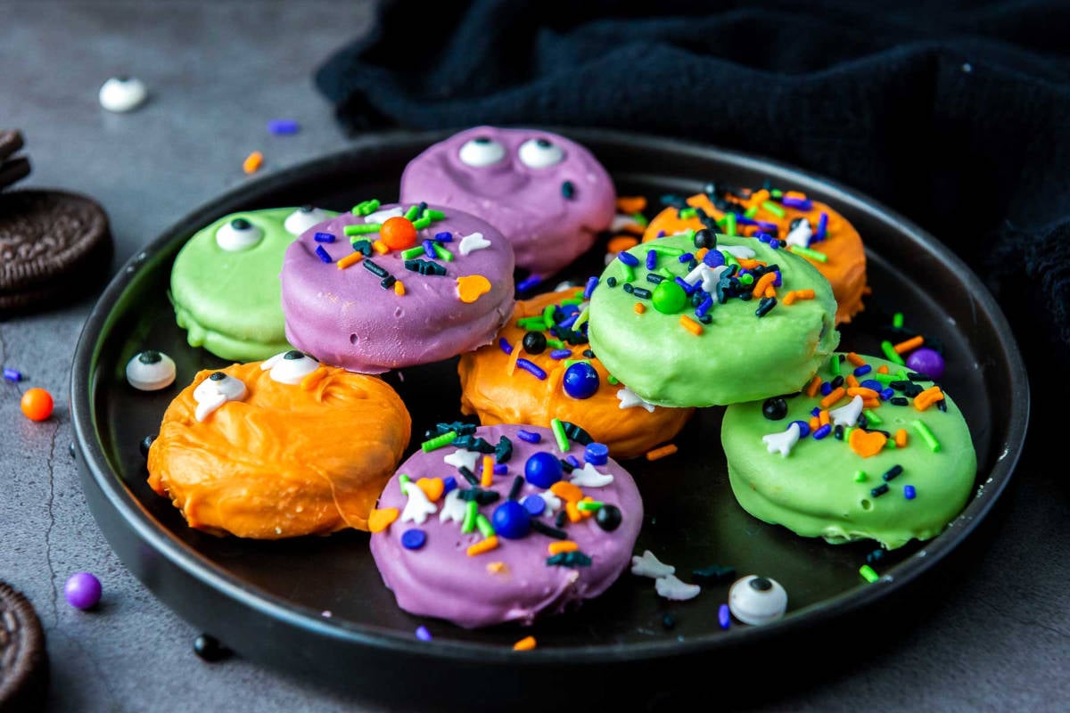 Black plate filled with orange, green, and purple Halloween Oreo cookies.