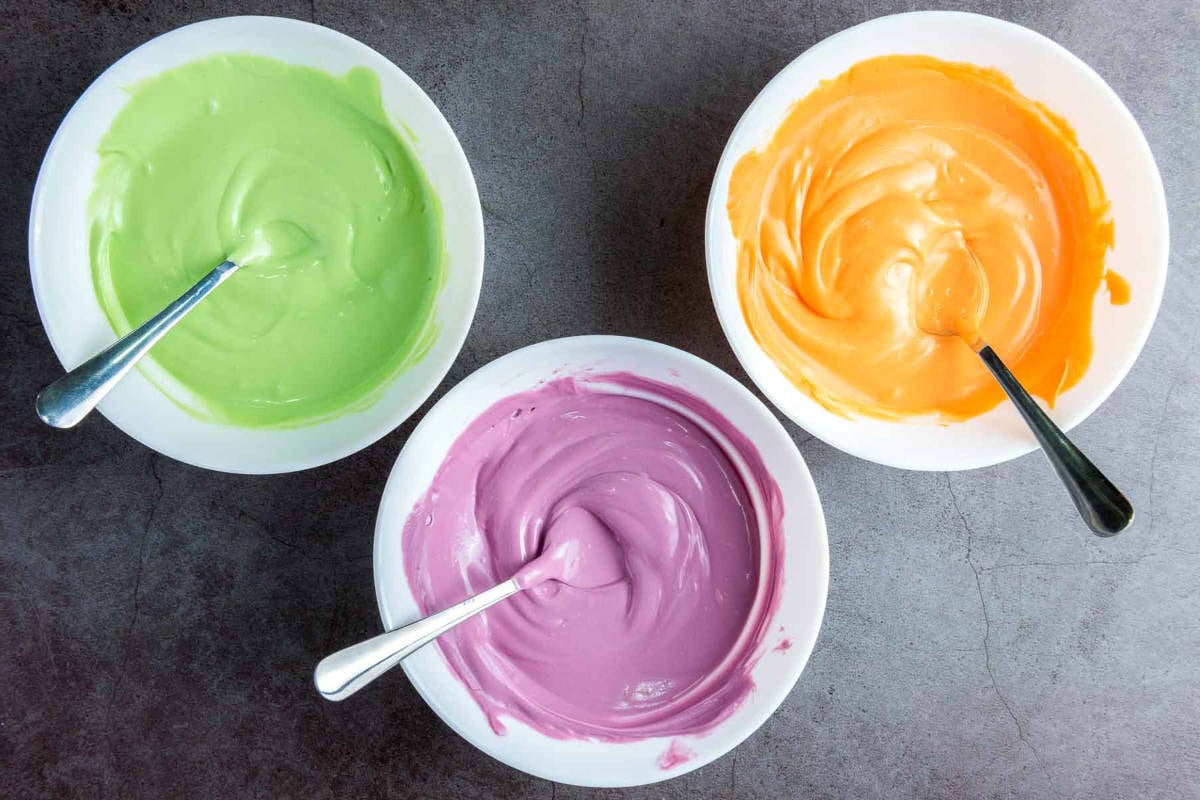 Melted orange, purple, and green candy coating in bowls with spoons.