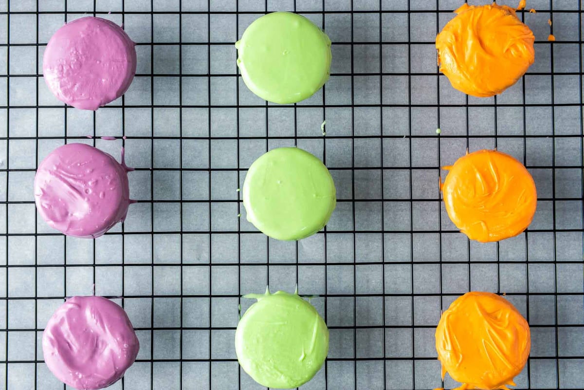 Oreos dipped in colorful melted candy coating set on wire rack.
