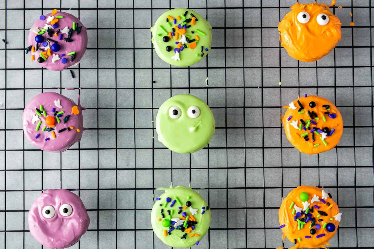 Decorated Halloween Oreo cookies on cooling rack with sprinkles and candy eyes.