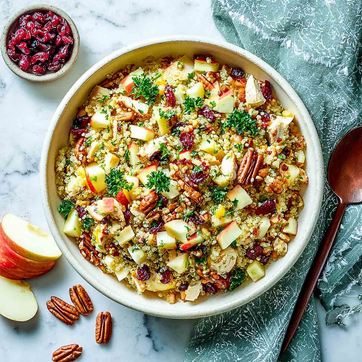 Quinoa salad with apples, cranberries, pecans, and chicken in a cream bowl.