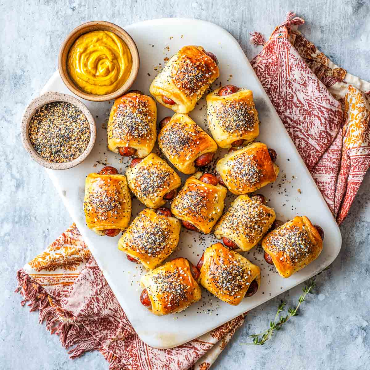 Golden mini pigs in a blanket sprinkled with everything bagel seasoning, served with mustard dip.