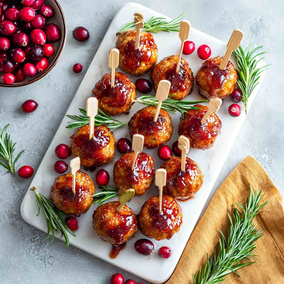 Mini turkey meatballs glazed with cranberry sauce and skewered with picks on a white platter.