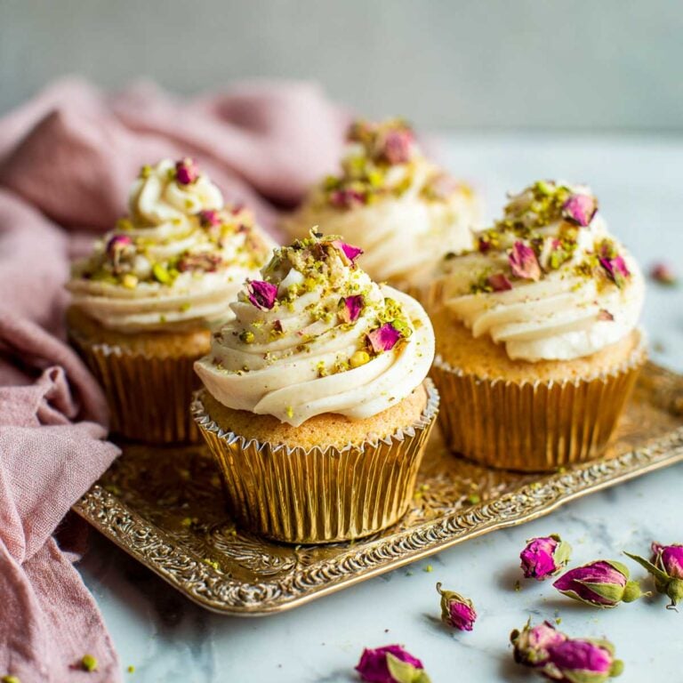 Eggless rose and pistachio cupcakes topped with rose-scented buttercream, crushed pistachios, and dried rose petals.