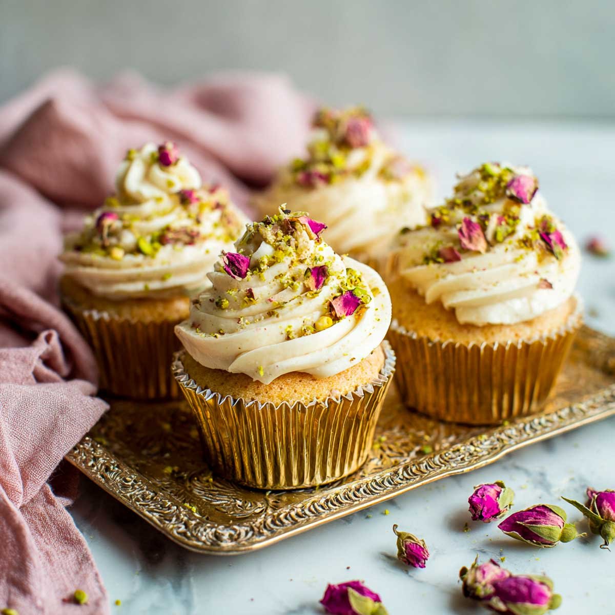 Eggless rose and pistachio cupcakes topped with rose-scented buttercream, crushed pistachios, and dried rose petals.