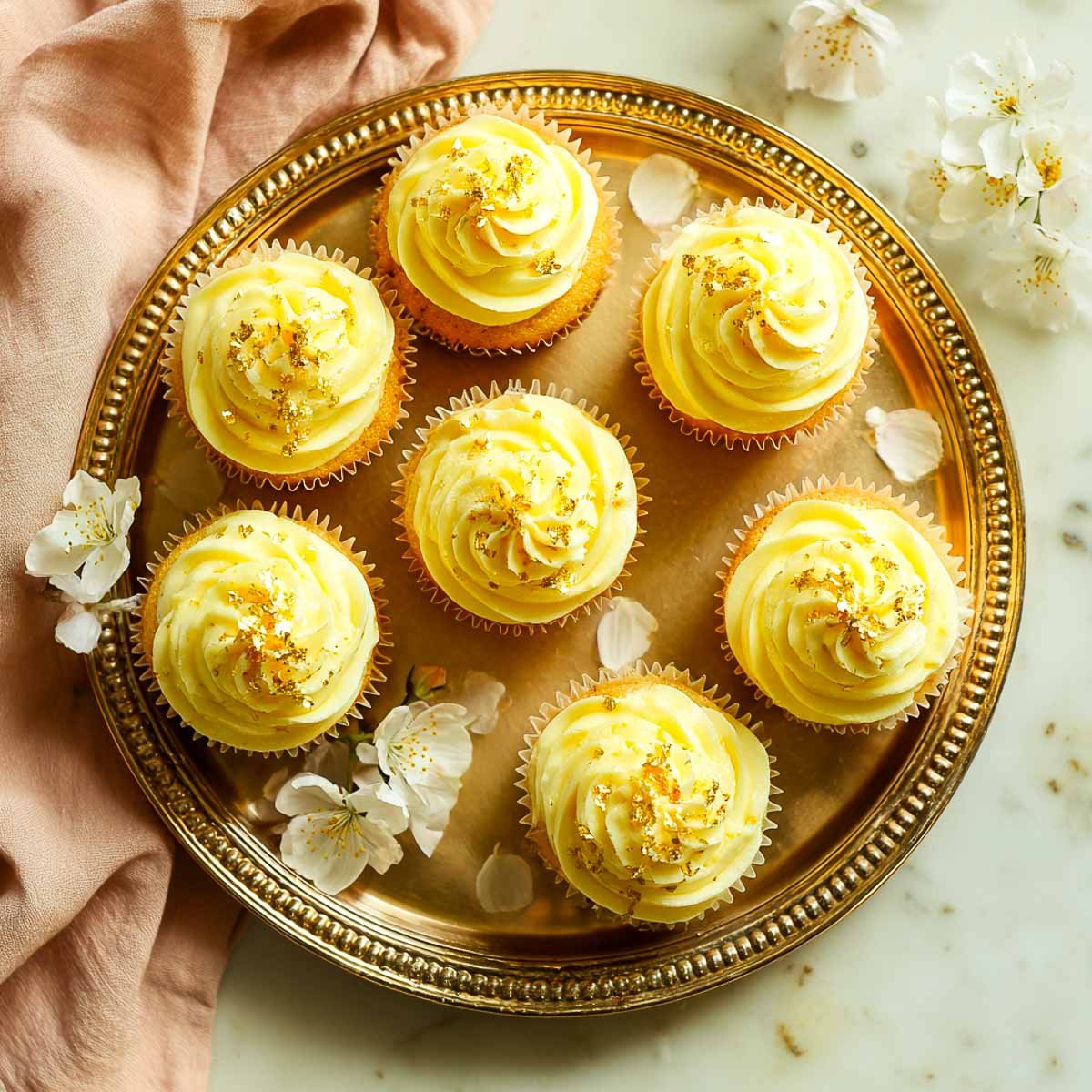 Tray of saffron vanilla cupcakes topped with gold leaf and frosting.