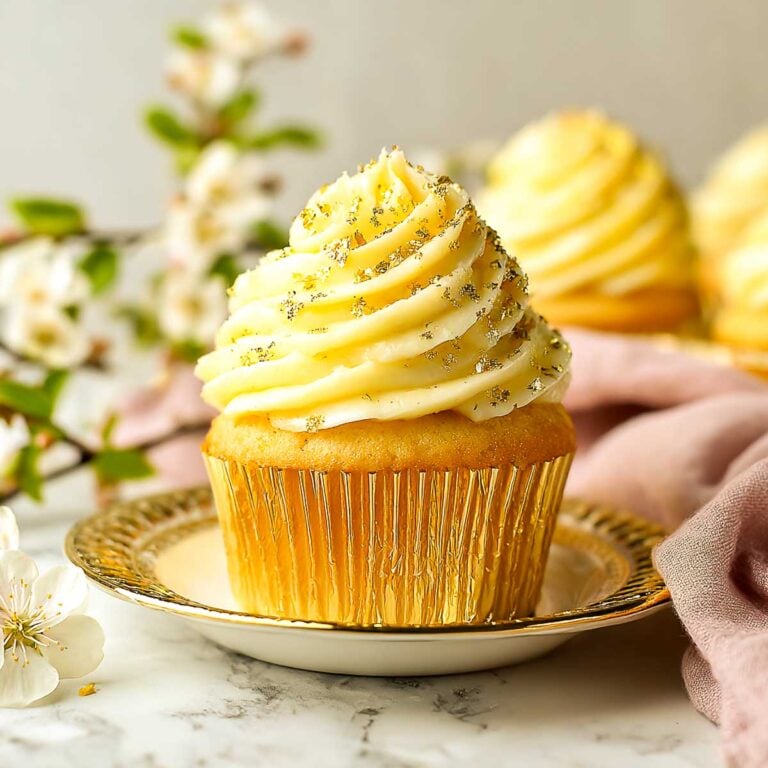 Elegant saffron vanilla cupcakes topped with creamy frosting and edible gold leaf, arranged on a festive platter.