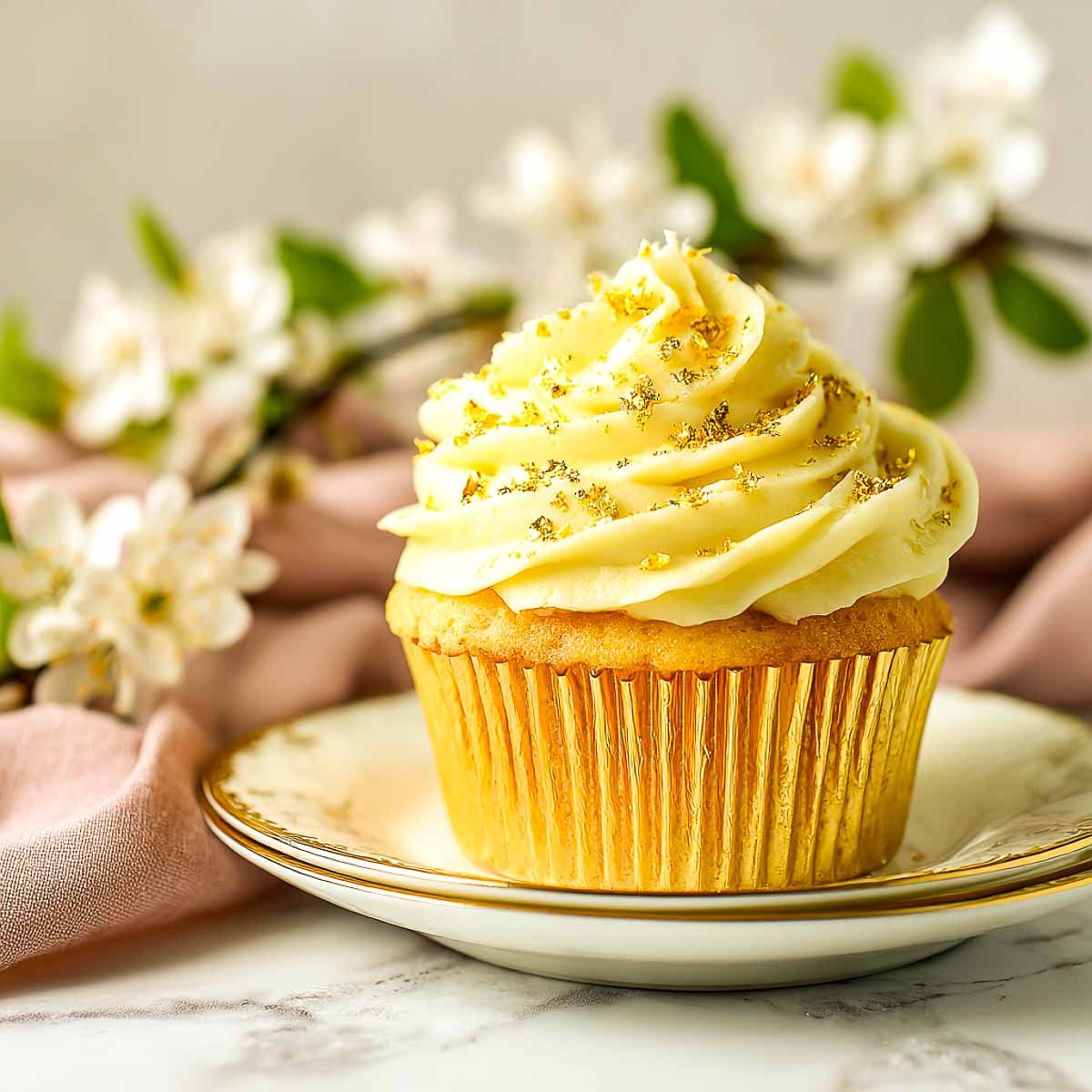 Single saffron vanilla cupcake with swirl frosting and gold leaf topping.