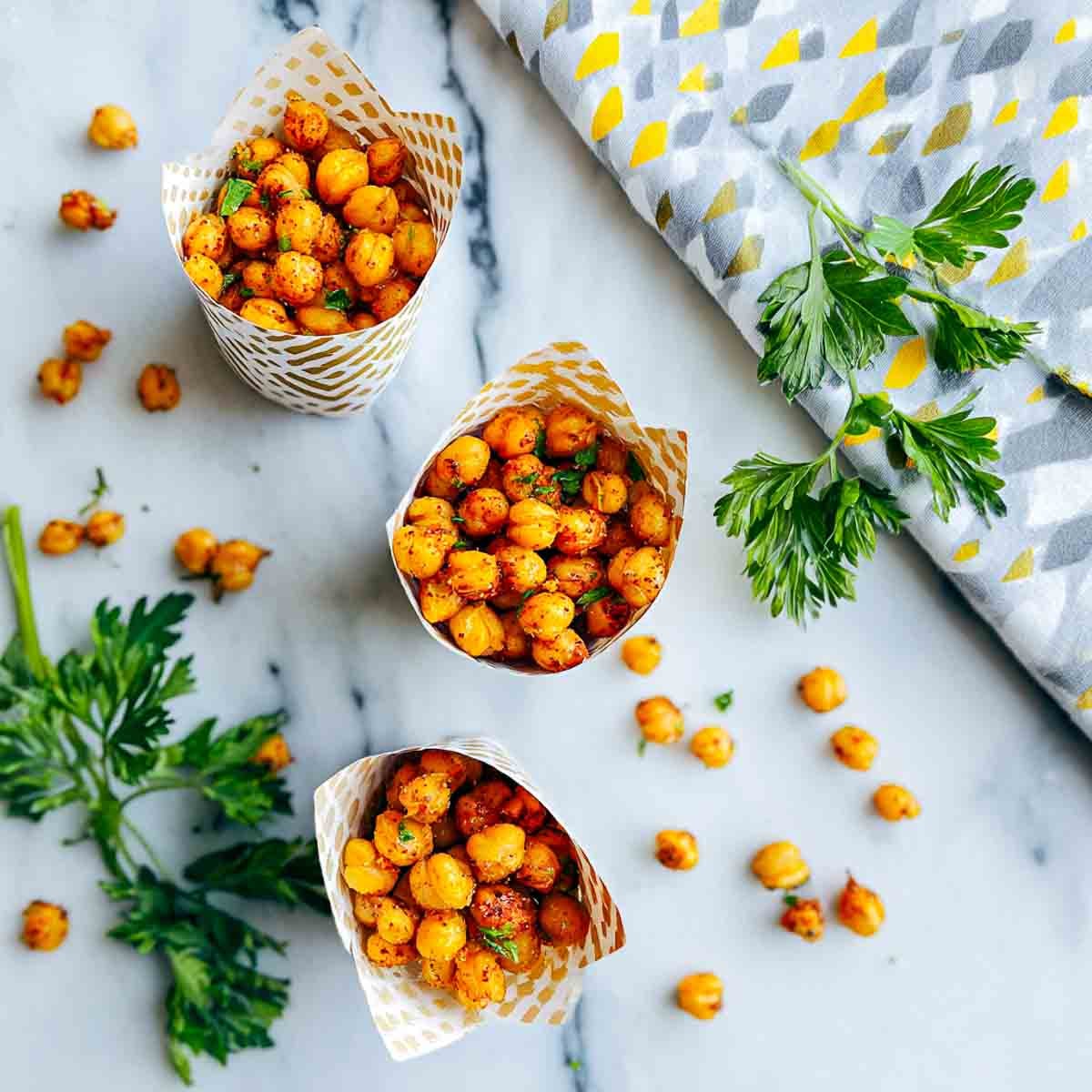 Paper snack cups filled with spiced roasted chickpeas on a marble surface with parsley.