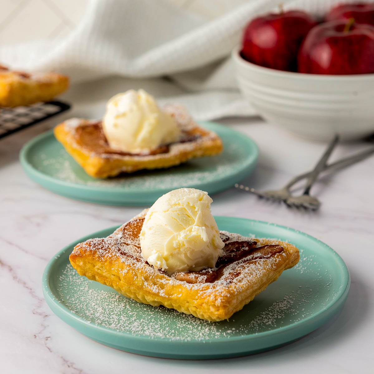 Upside down apple tart topped with a scoop of vanilla ice cream and dusted with powdered sugar on a teal plate.