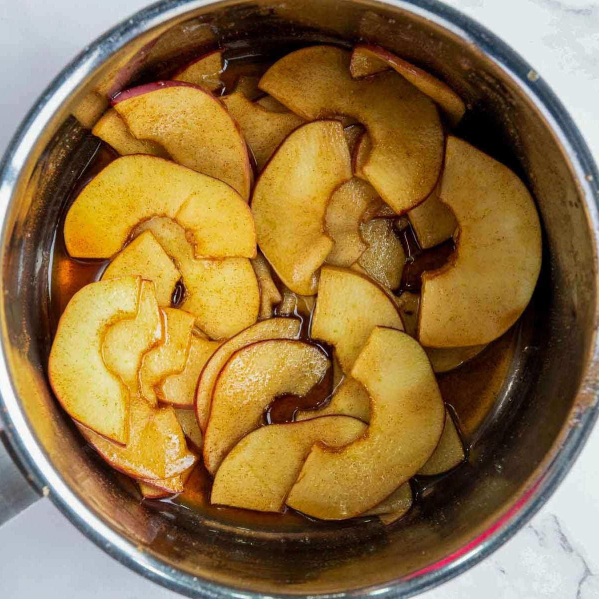 Apple slices simmering in a saucepan with butter, sugar, and cinnamon.